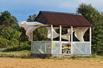 Dramatic abandoned empty gazebo with disheveled curtains flutter in the strong wind on a summer...