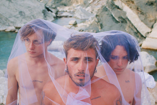 Three shirtless men covered with white tulle veil