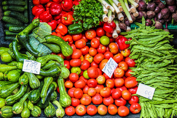 Fresh vegetables on the farmers market. Handwritten papers in Portuguese with names of the vegetable sorts and prices. Organic food. Red tomatoes, green zucchinis, red peppers, garden cucumbers