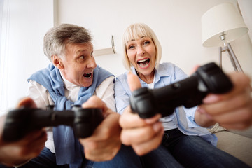 Overjoyed elder couple playing video games at home © Prostock-studio
