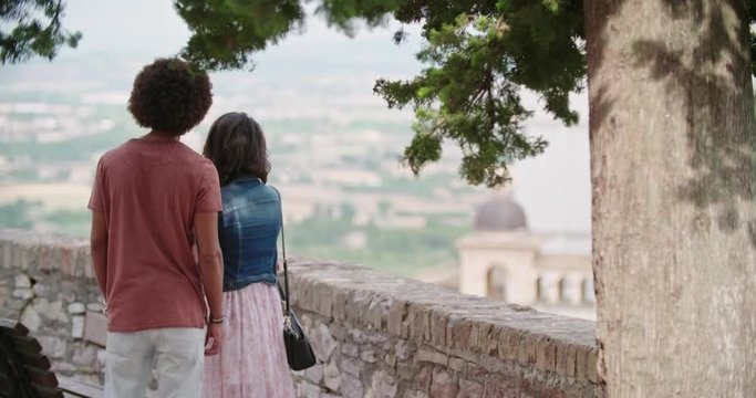Back view of romantic couple looking at viewpoint in rural town of Assisi.Portrait medium shot.Friends italian trip in Umbria.4k slow motion