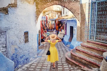 Abwaschbare Fototapete Marokko Buntes Reisen durch Marokko. Junge Frau im gelben Kleid zu Fuß in der Medina der blauen Stadt Chefchaouen.