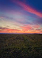 Majestic autumn sunset over a countryside open field. Soft and colorful clouds over empty plain land.