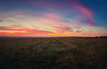 Majestic autumn sunset over a countryside open field. Soft and colorful clouds over empty plain land.