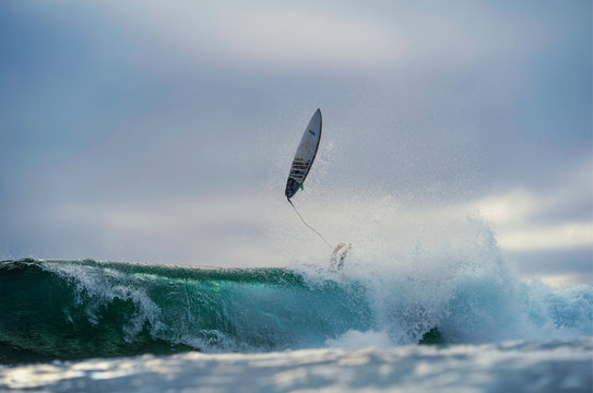 Surfer falling off wave with surfboard in the air