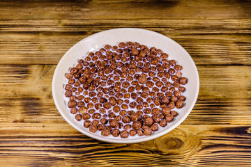 Ceramic plate with chocolate cereal balls in milk on wooden table