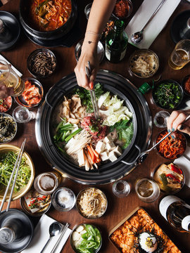 Overhead View Of Hands Reaching For Asian Food On Table