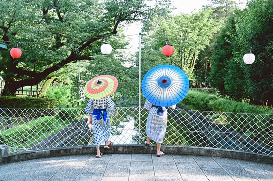 Rear view of siblings with parasols standing near chainlink fence