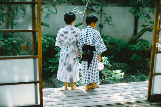 Rear view of siblings in kimono standing on patio