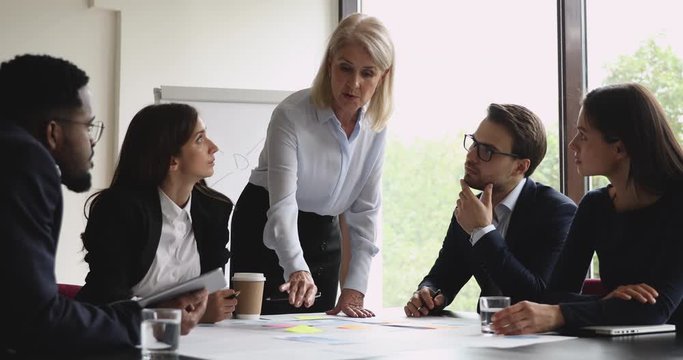 Senior businesswoman mentor teach young workers explain paperwork in office