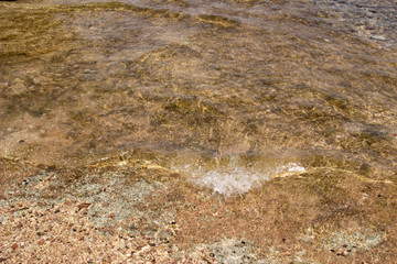 Summer background of hot sand with sea or ocean wave bubbles with copy space for card or advertisement at dawn or sunset