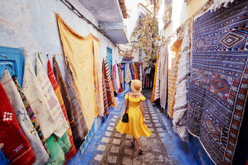 Fototapeta na wymiar Colorful traveling by Morocco. Young woman in yellow dress walking in medina of blue city Chefchaouen.