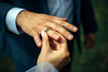 Young bride put a gold wedding ring on the groom's finger, close-up. Wedding ceremony, exchange of rings.