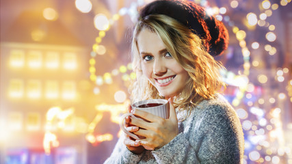 Pretty woman drinks mulled wine at the Christmas market at night