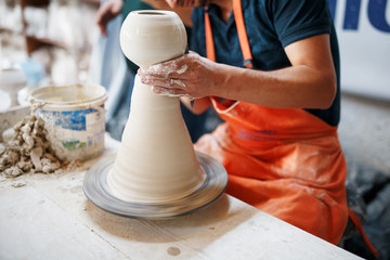 Hands of young potter, was produced on range Hands of a potter skillfully making a pot of white...