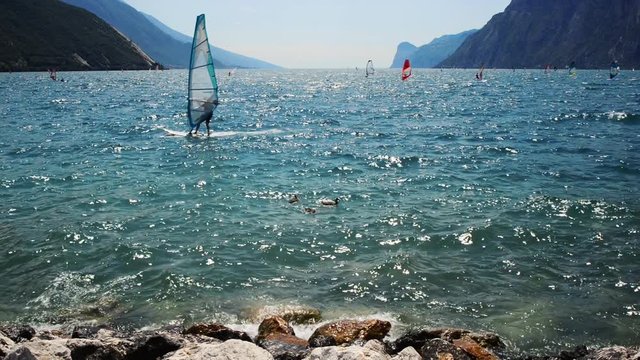 Windsurfing and paddleboarding on Lake Garda in Torbole resort. Windsurfer Surfing The Wind On Waves, Recreational Water Sports