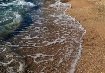 Summer background of hot sand with sea or ocean wave bubbles with copy space for card or advertisement at dawn or sunset