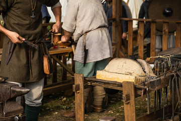 Reconstruction of old crafts. A craftsman in historical clothing bends an iron rod with metal tongs. A blacksmith forges a metal product. Dressed in an old outfit. Ancient metallurgy.