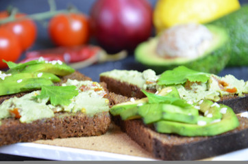 Guacamole with bread and avocado Sandwich with avocado and guacamole. Black cereal bread. Ingredients for making lime, red pepper, tomatoes. Healthy food, diet on a black background