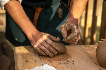 Reconstruction of an ancient craft. Artisan squeezes clay to create pottery. Workshop. Hands occupied by modeling. Teaches pottery art. Shows how to sculpt on the table. Dressed in an old outfit.