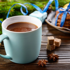 Christmas background of blue hot chocolate mug, spruce branch and tray with gingerbread cookies on wooden table