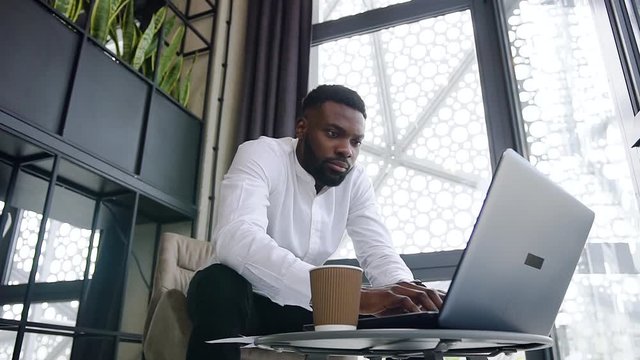 Attantive clever dark-skinned office worker with well-groomed beard working at the computer in the special separate place in the office