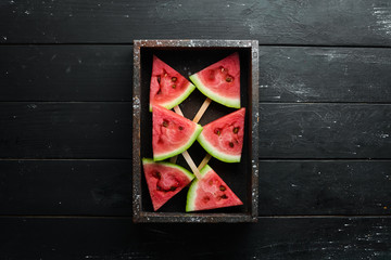 Watermelon popsicle on black background. Watermelon slices on sticks. Top view. Free copy space.