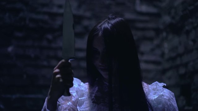 Crazy killer looking at sharp knife in darkness, insane smile on face, horror