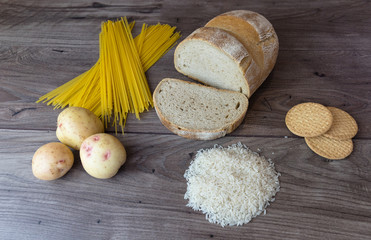 Common bad carbohydrates to avoid such as white bread, pasta, rice, potatoes and buscuits laying on top of a wooden table viewed from above