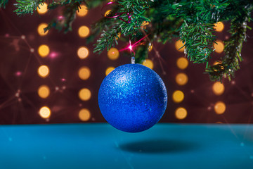 There is blue ball on the green xmas tree branch. There are glowing lights/bokeh and pink stars on the background. Merry Christmas. Happy New Year 2020. 