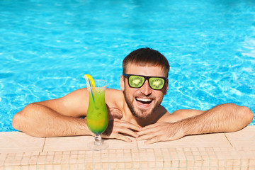 Young bearded man with refreshing cocktail in swimming pool at resort