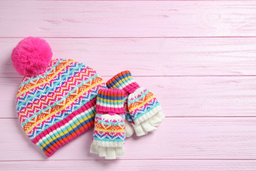 Fototapeta na wymiar Warm knitted hat and mittens on pink wooden background, flat lay. Space for text
