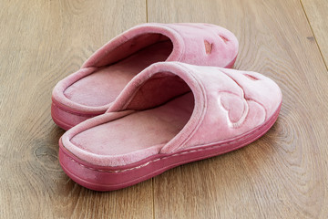 Pair of pink female house slippers on a brown wooden floor. Cozy, warm and comfortable domestic shoes.
