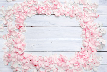 Frame made of light pink rose petals on white wooden background. Top view. Valentine's background. Copy space.