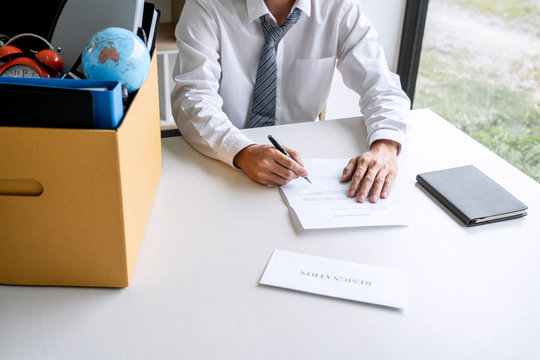 Images Of Packing Up All His Personal Belongings And Files Into A Brown Cardboard Box, Businessman Has Stress To Resignation And Signing Cancellation Contract Letter In Office, Resign Concept