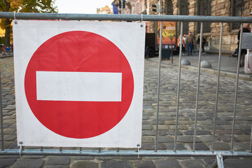 Stop sign hanging on a metal fence. In the frame you can see a cobblestone road.
