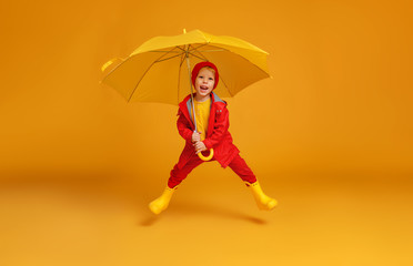 happy emotional cheerful child boy jumping and laughing  with red umbrella   on colored yellow background.