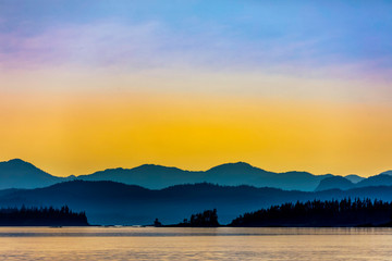 Fototapeta na wymiar Yellow Sunset over Mountains, Ocean, Silhouetted