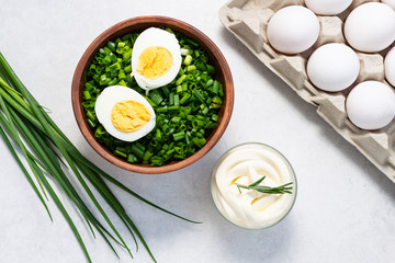 Fresh organic salad with green onions, eggs, creamy sauce and crackers on white marble table top view.