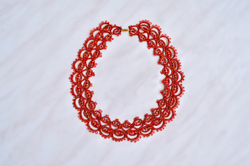 Wicker bracellet or necklace in red and gold colors. Lacy weave. Tatting. Handmade jewelry made of mercerized cotton or silk with beads. Marble background.