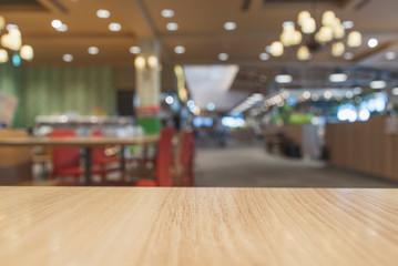 Empty light colored wood table top and blur of food court/restaurant background/selective focus. For montage product display.