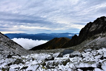 Fototapeta na wymiar Mountain lake among snowy stones against the background of mountain ridge and white blue sky.