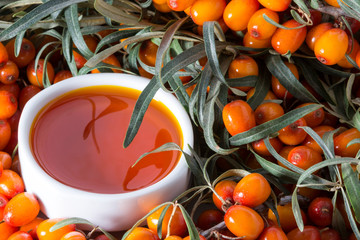 White cup with sea buckthorn oil on the background of sea buckthorn berries