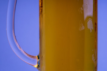 A misted glass of beer on a blue background. Close-up.