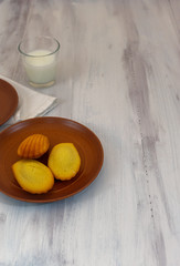 Madeleines and milk in wooden rustic background with copy space in portrait position 