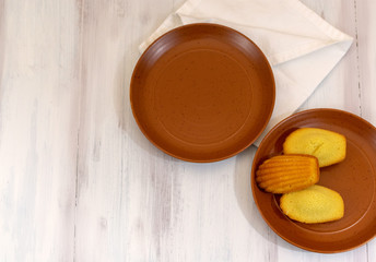 Top view of empty terracotta plate and madeleines, over wooden rustic background with copy space 