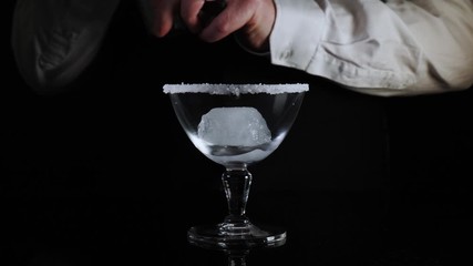 Bartender pours a classic yellow cocktail margarita drink in an elegant glass with ice isolated against black background - Powered by Adobe