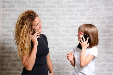 Lifestyle Concept -Adorable woman and girl with beautiful  hair chatting or using internet on cell phone over white brick wall background. Portrait of attractive happy girl holding smartphone.