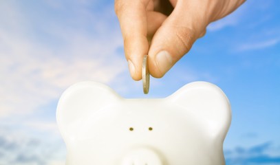 Hand putting coin to piggy bank and coins on white background