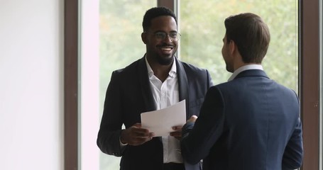 Two happy diverse businessmen talking laughing handshaking standing in office - Powered by Adobe